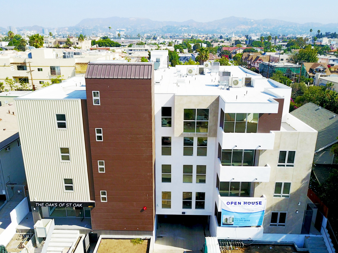 A building exterior picture of 5-story condominium. Metal panel and brown stucco finish. White balconies at the front.