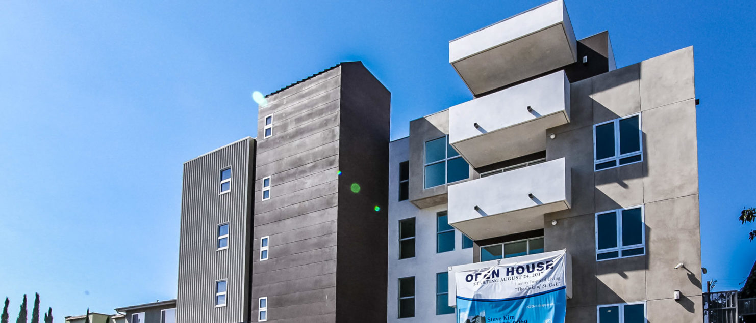 A building exterior picture of 5-story condominium. Metal panel and brown stucco finish. White balconies at the front.