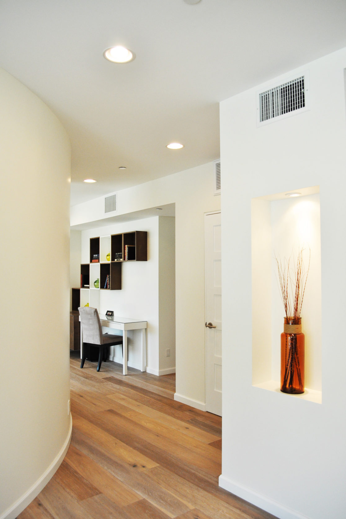 A building interior picture of the corridor. wood floor and white wall.