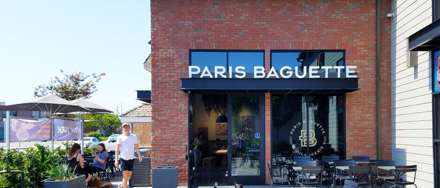 A building exterior picture of paris baguette store with outdoor seating. Brick exterior wall and white exterior siding wall.