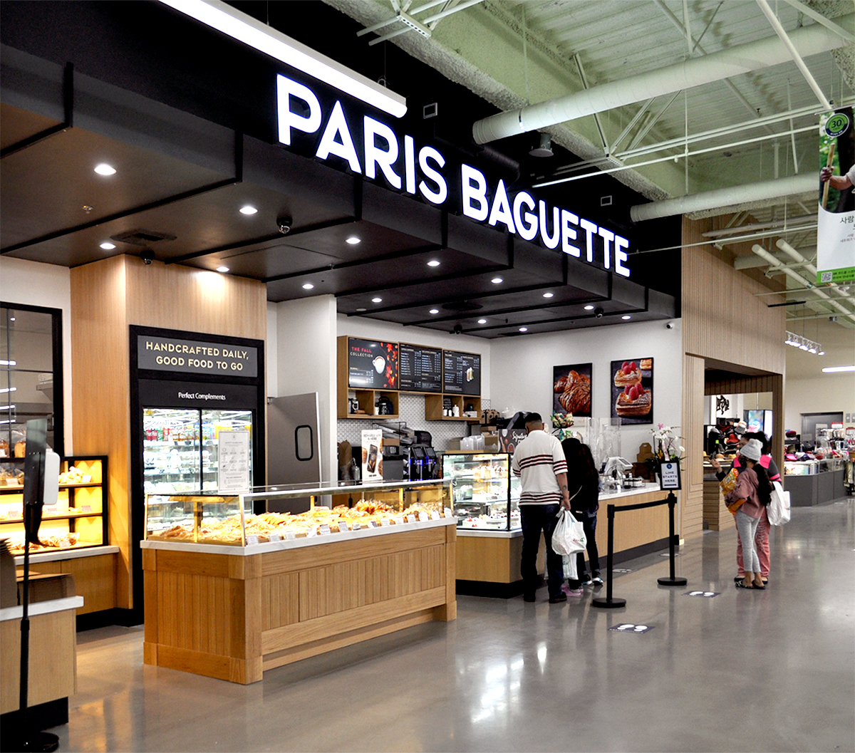 A building interior picture of paris baguette store. Bread display cases at the front and casher counter behind. Concrete floor and black ceiling.